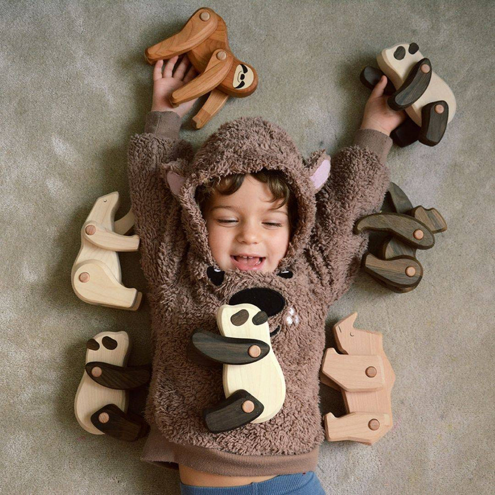 Bajo- Child laying on the floor playing with various wooden animal figures, including the Sloth, Panda, and Polar Bear- Bela Luna Toys