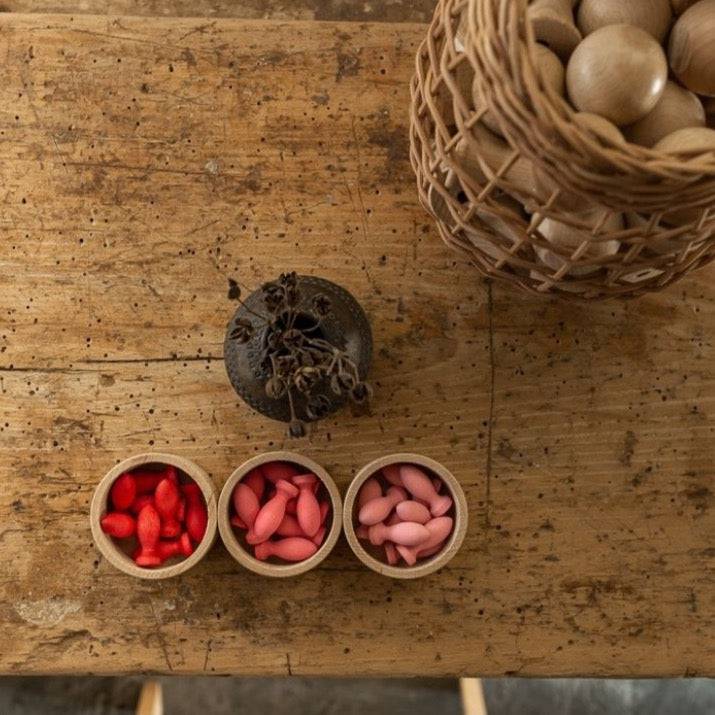Grapat Flower Petals sorted by color -- red, darker pink, lighter pink -- in little bowls on a rustic wooden table