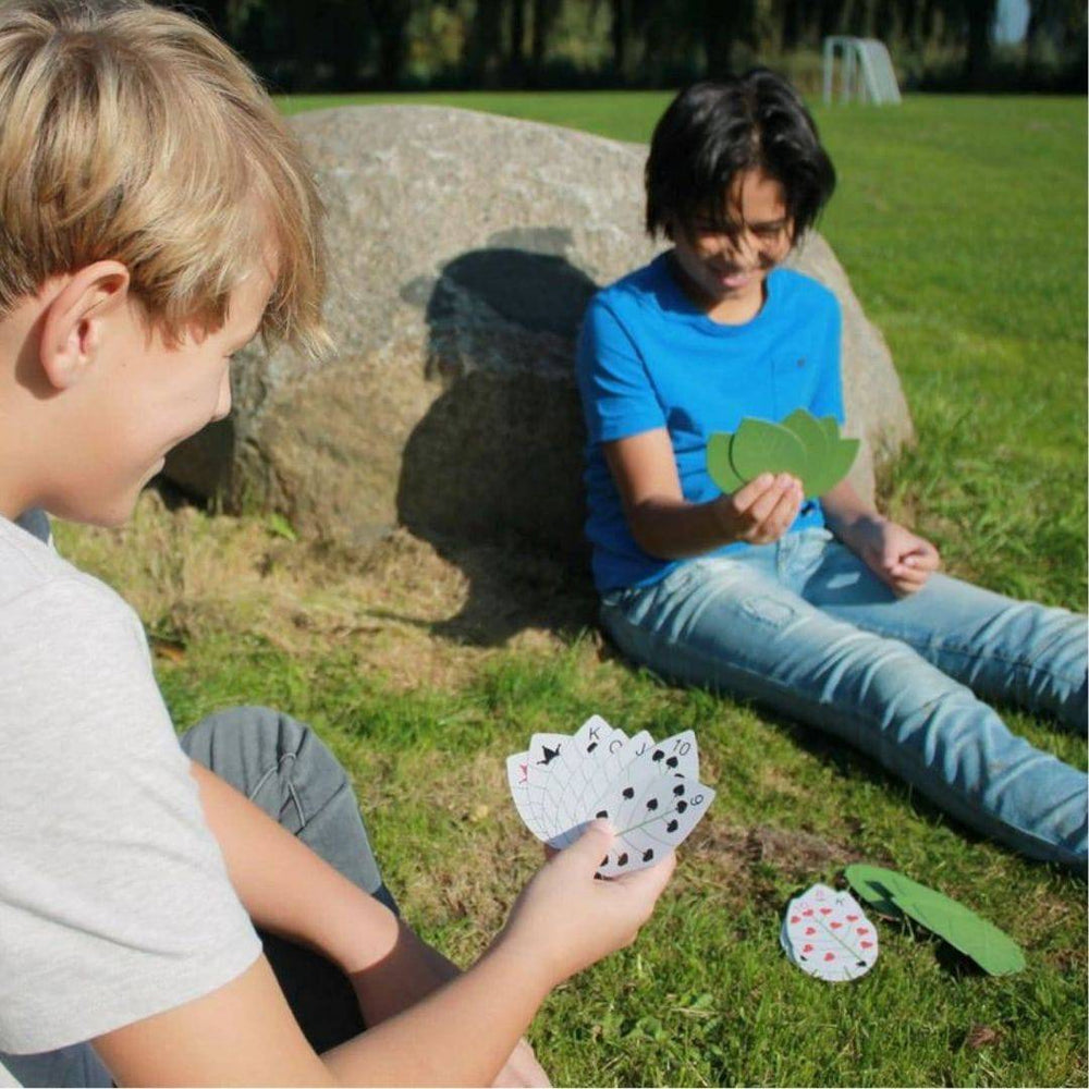Two kids playing card game with Leaf Cards outside on grass