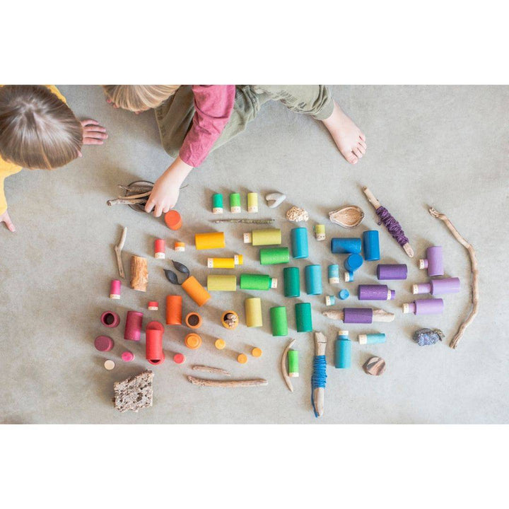 Overhead view of two children playing with Lola set on floor, along with some small sticks and items from nature