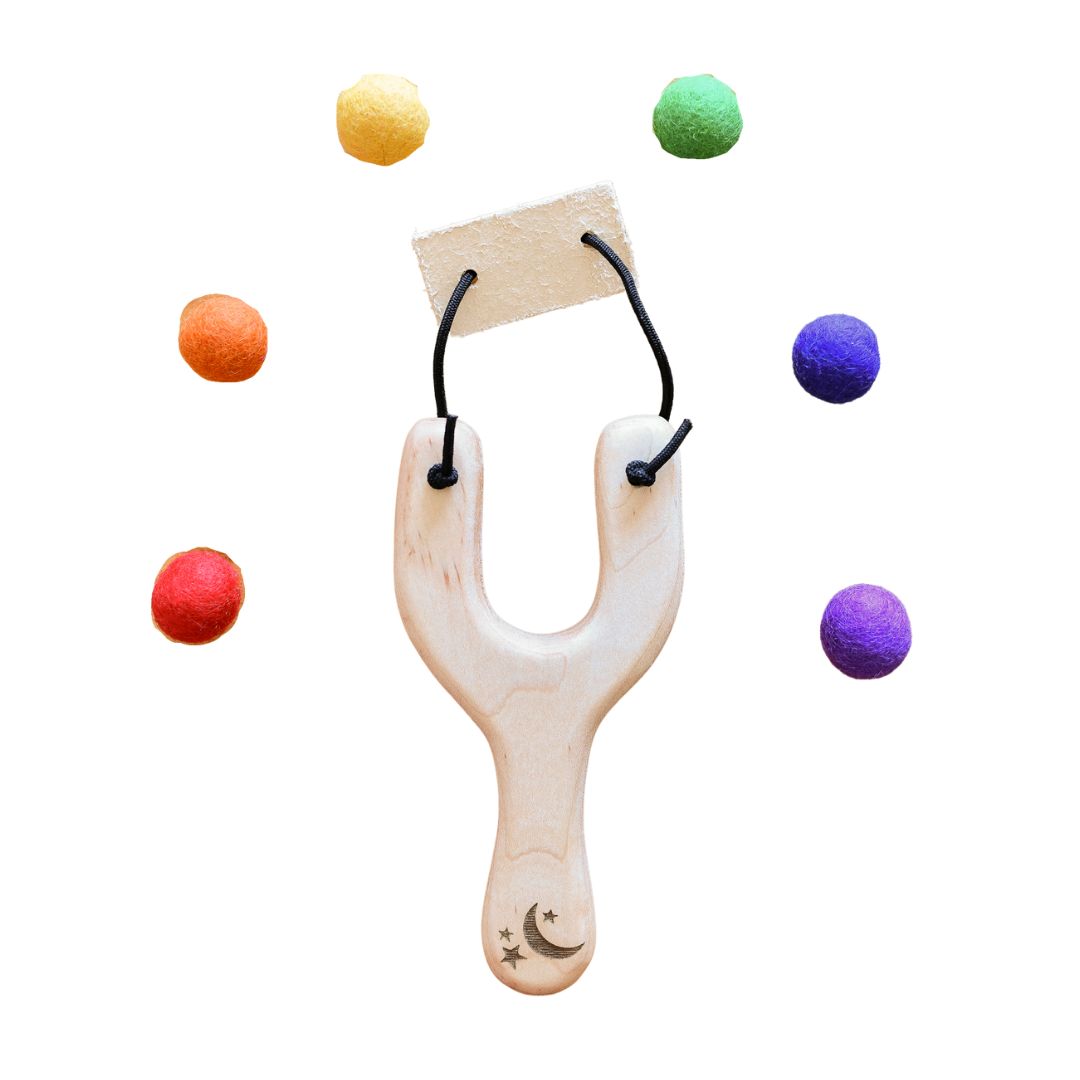 Wooden slingshot with stars and moon carved into base of handle, surrounded by colorful felt balls- Bella Luna Toys
