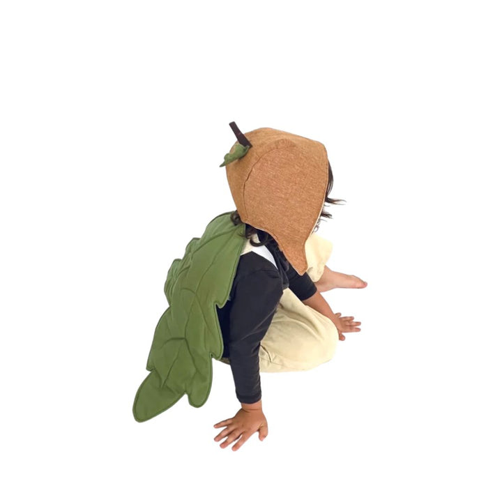 Child wearing Jack Be Nimble brown acorn hat with green oak leaf wings while sitting on floor- Bella Luna Toys