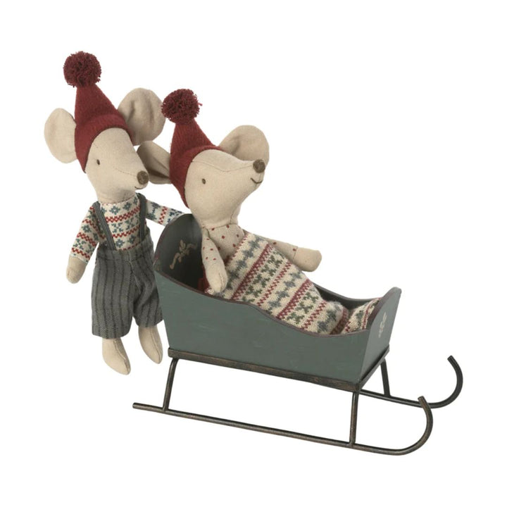 Maileg Sleigh, Mouse -  Two stuffed toy Christmas mice with red pom pom hats, Christmas sweaters. One mouse is tucked into green wooden sleigh with blanket, and the other is standing outside of sleigh -  Bella Luna Toys