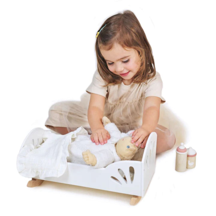 Child playing with doll laying in Tender Leaf Toys wooden bed, with wooden bottles to the side- Bella Luna Toys